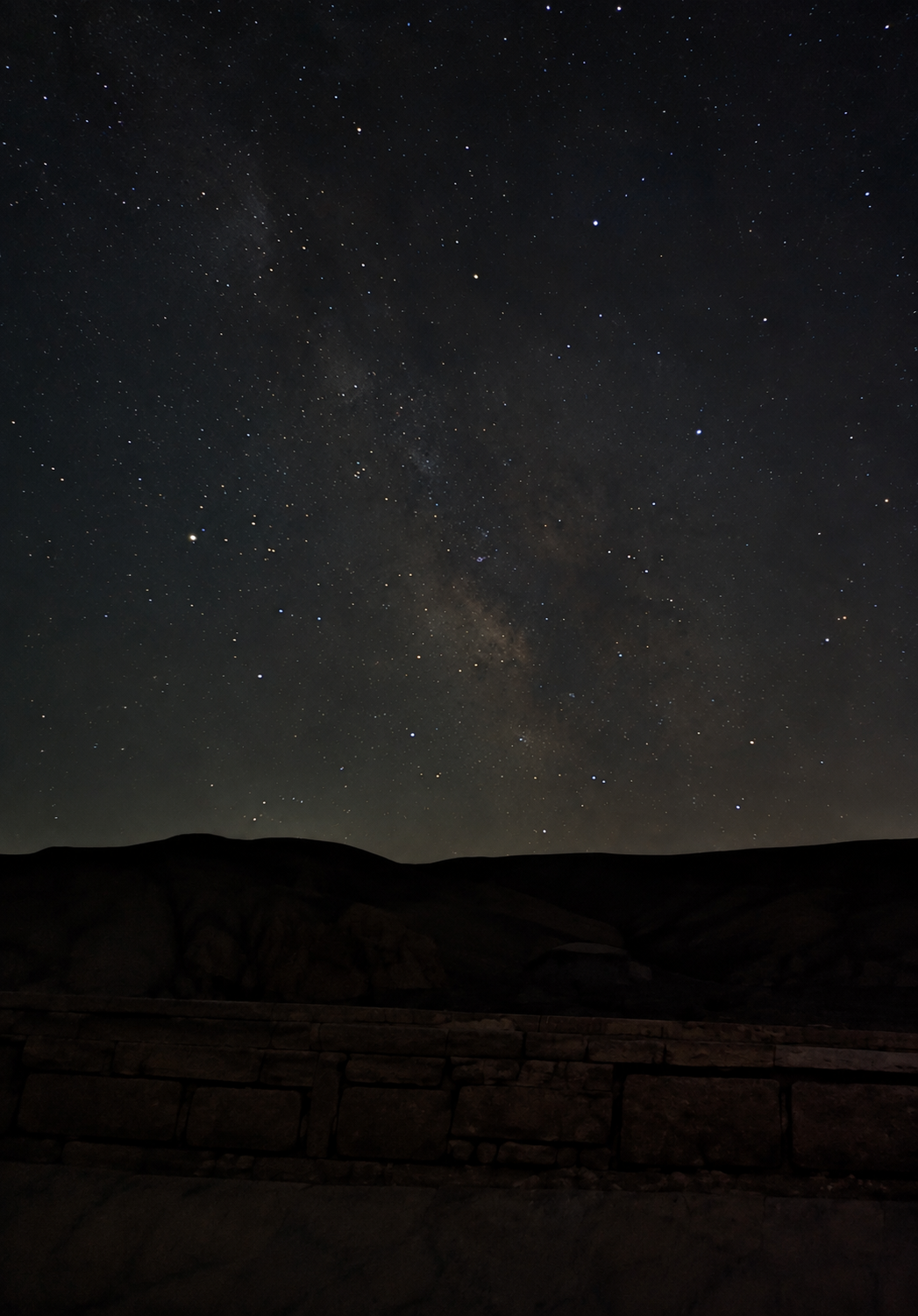 Milky Way rising over a stone wall and dark hills